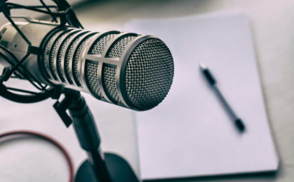 An image of a podcast microphone with a notebook and pen resting in the background
